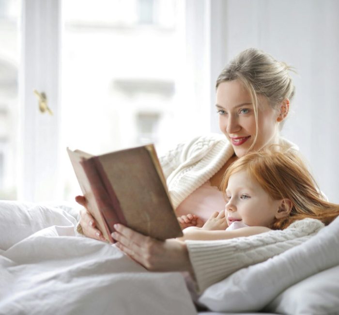 A mother and daughter enjoying a cozy moment reading together in a bright bedroom.