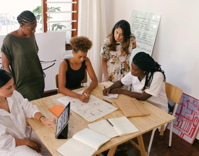 Diverse team collaborates on a project using digital and paper resources in a bright office.