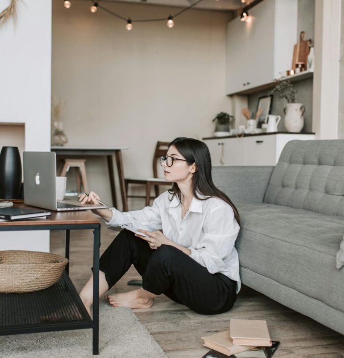 Asian woman working on laptop from cozy living room, showcasing modern home office setup.
