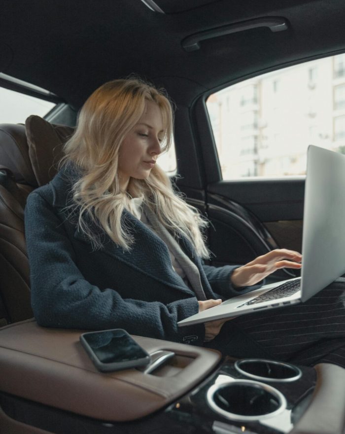 Businesswoman working remotely on a laptop in the backseat of a luxury car. Stylish, modern, and focused.