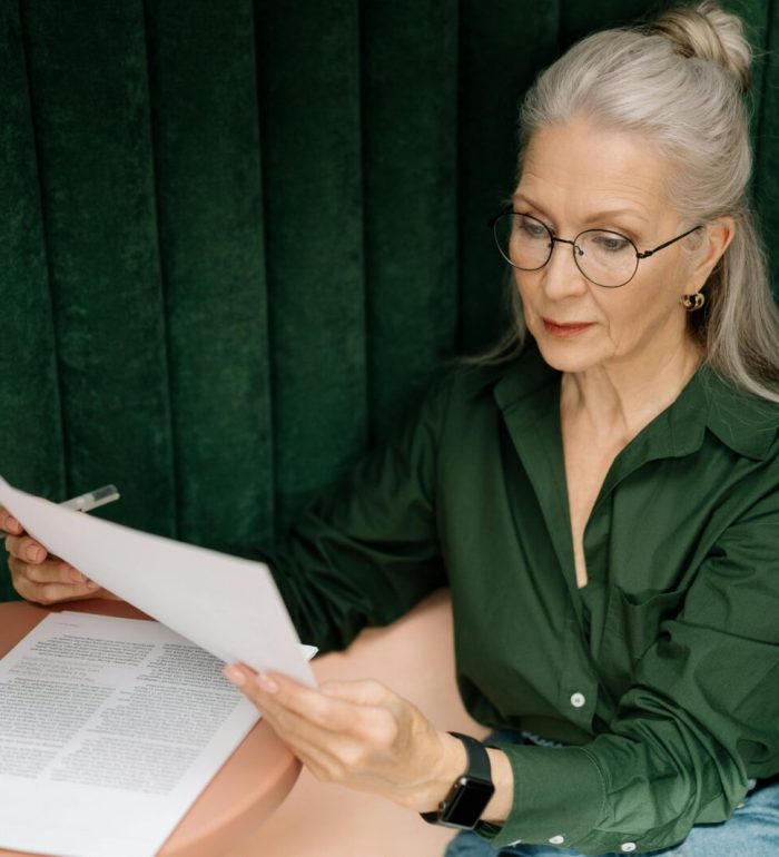 Senior woman wearing glasses, reading documents at a desk indoors, showcasing professional focus.